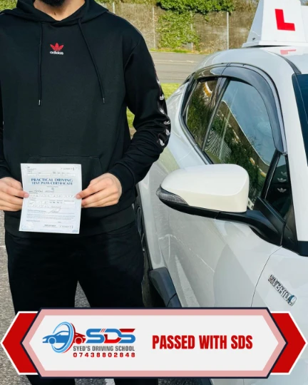 Successful learner holding a practical driving test pass certificate beside a learner car