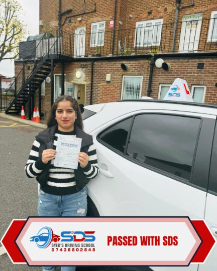 Successful learner standing beside a white tuition car with a pass certificate