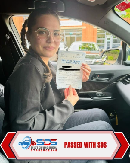 Successful learner holding a practical driving test pass certificate inside a car