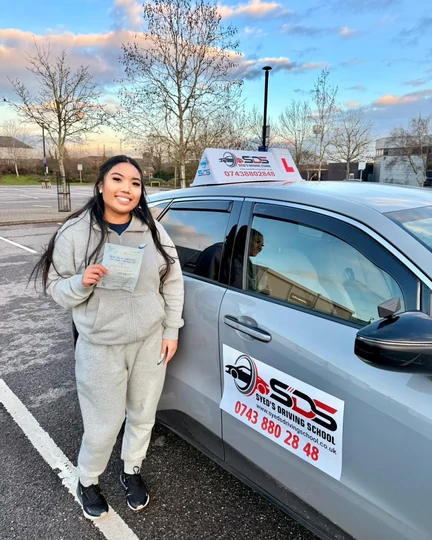 Successful learner celebrating a practical driving test pass beside a Syed’s Driving School tuition car