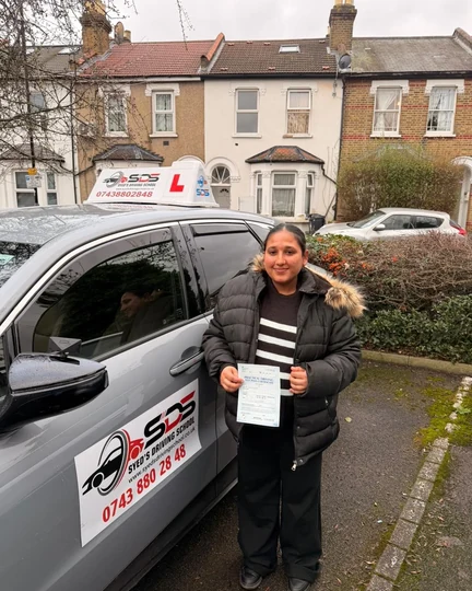 Successful learner celebrating a practical driving test pass beside a Syed’s Driving School tuition car
