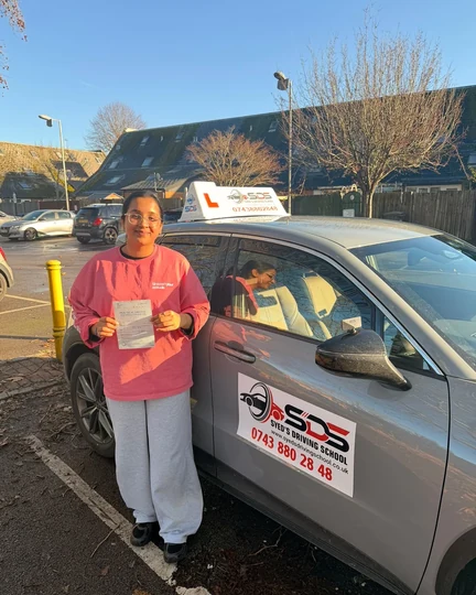 Successful learner celebrating a practical driving test pass beside a Syed’s Driving School tuition car