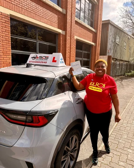 Successful learner celebrating a practical driving test pass beside a Syed’s Driving School tuition car