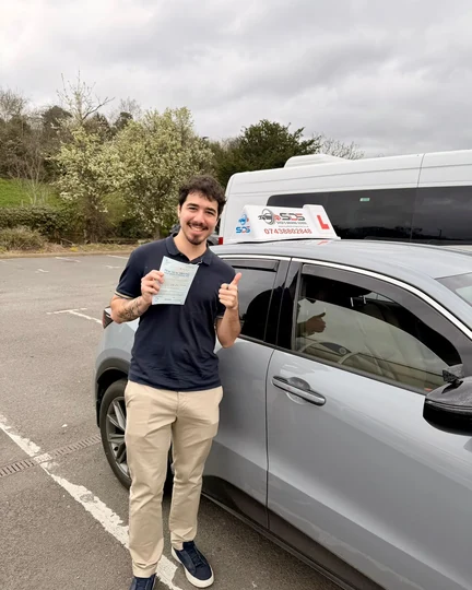Successful learner celebrating a practical driving test pass beside a Syed’s Driving School tuition car